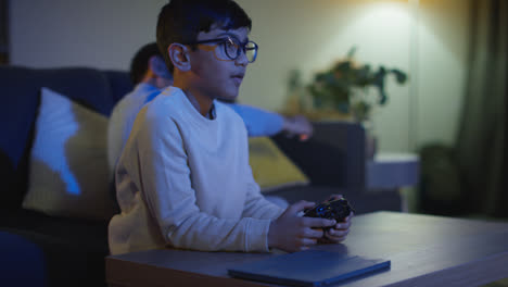 Two-Young-Boys-At-Home-Having-Fun-Playing-With-Computer-Games-Console-On-TV-Fighting-Over-Controllers-Late-At-Night-5